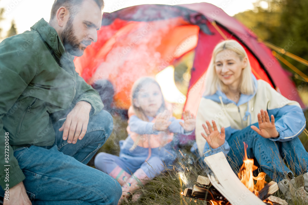一对年轻的成年夫妇和一个小女孩坐在一起，在篝火旁玩得很开心，带着帐篷在大自然中旅行
