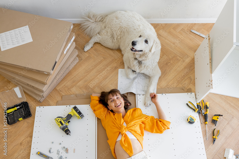 一个年轻快乐的女人和她的可爱的狗躺在地板上，一边休息，一边修理新公寓。