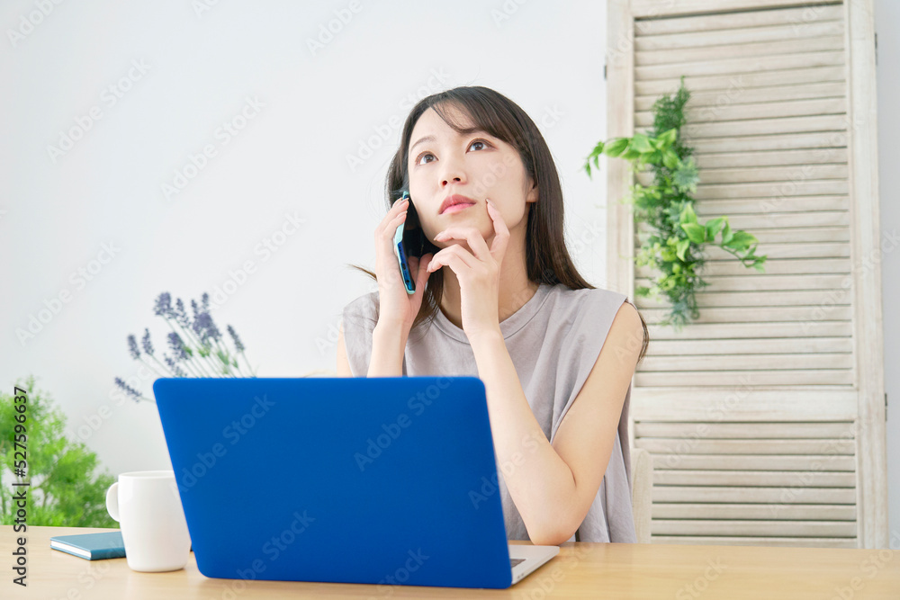 リビングでノートパソコンの前でスマホで電話する女性