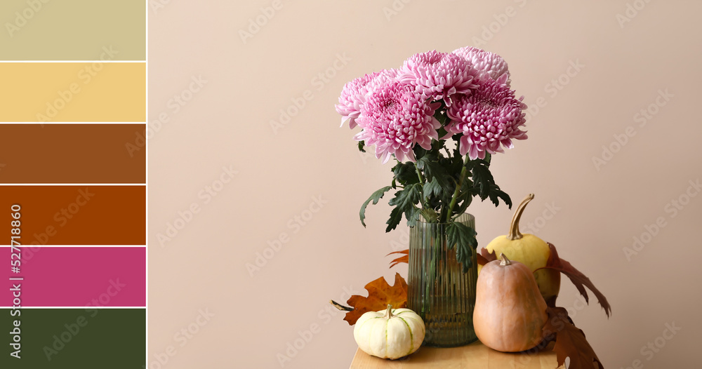 浅背景下，桌上摆放着粉红色菊花、秋叶和南瓜的花瓶。