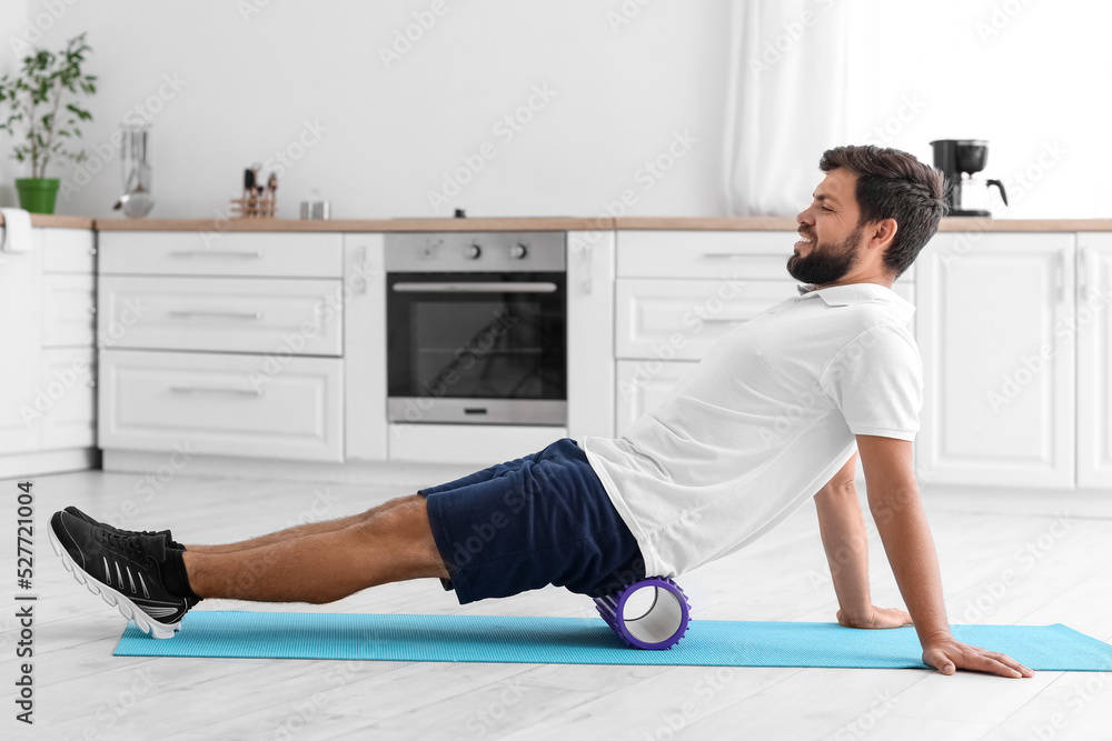 Young man training with foam roller in kitchen