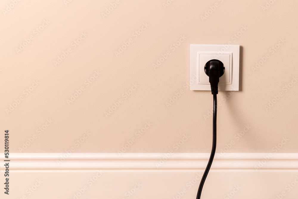 现代米色墙上插入黑色插头的白色欧洲电源插座