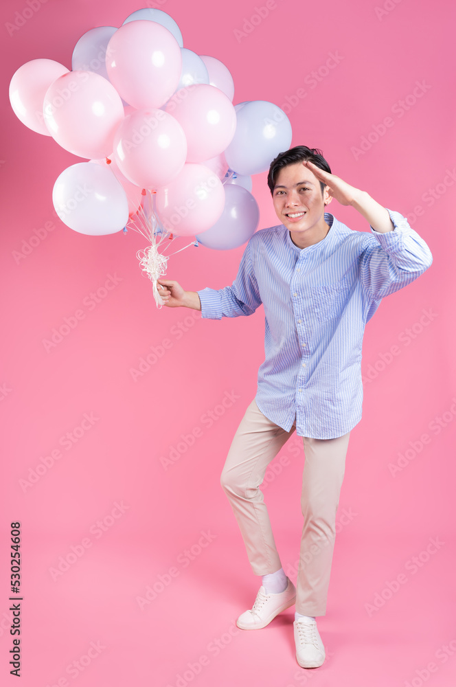 粉红色背景下拿着气球的亚洲年轻人