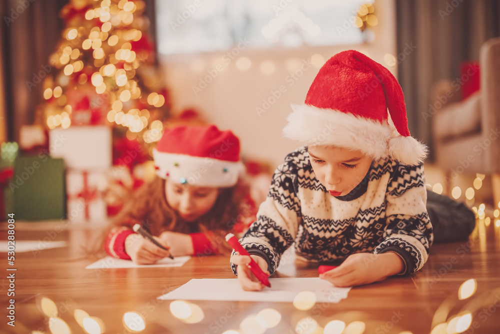 Children lying on the floor indoors and writing letters for Santa Claus.