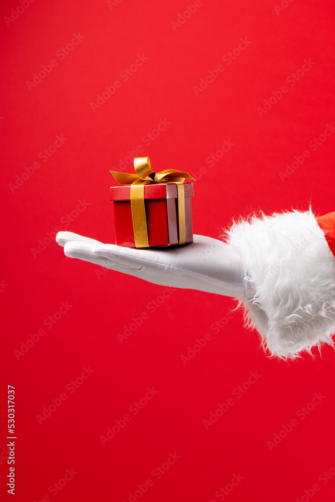 圣诞老人的手拿着圣诞礼物，红色背景上有复制空间的图像