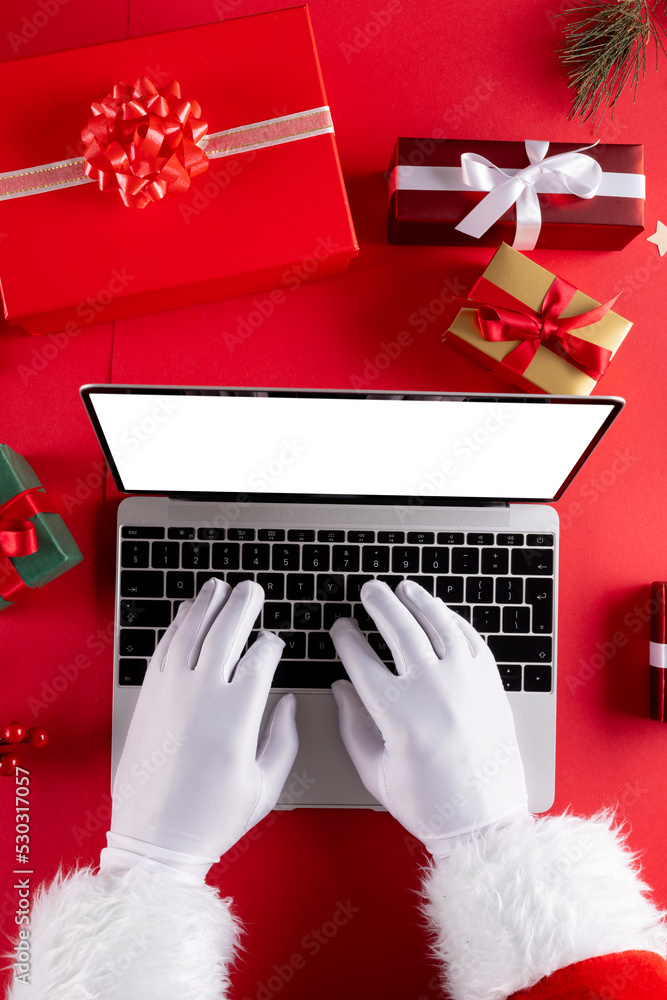 圣诞老人使用笔记本电脑的手的图像，屏幕为空白，红色背景为礼物