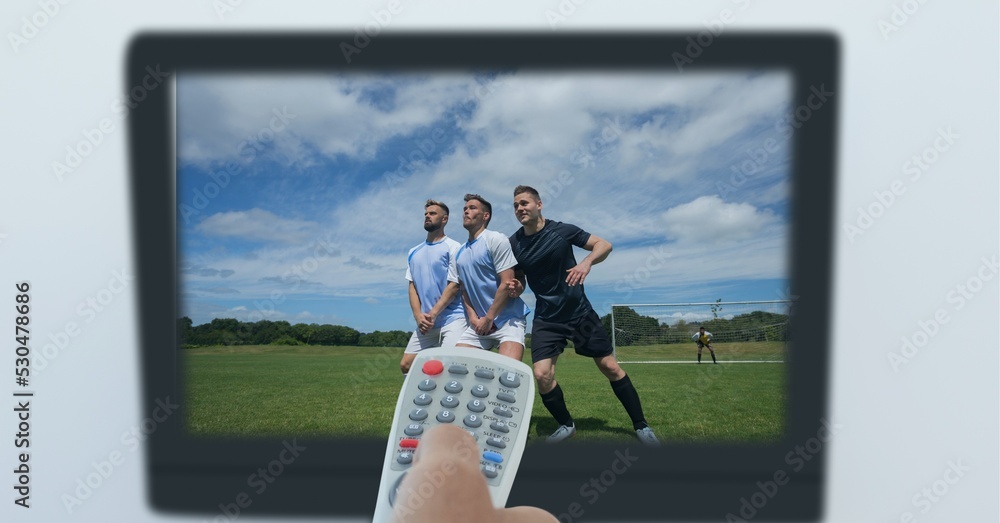 体育迷手持遥控器的手的组成，电视屏幕上有足球比赛