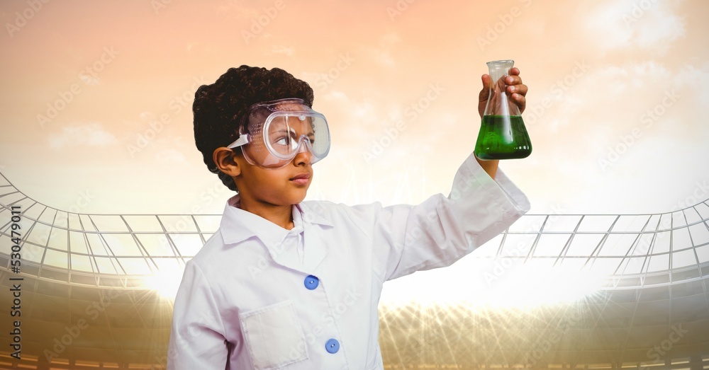 穿着实验服的男孩拿着一个化学烧瓶对着有复制空间的体育场的合成图像