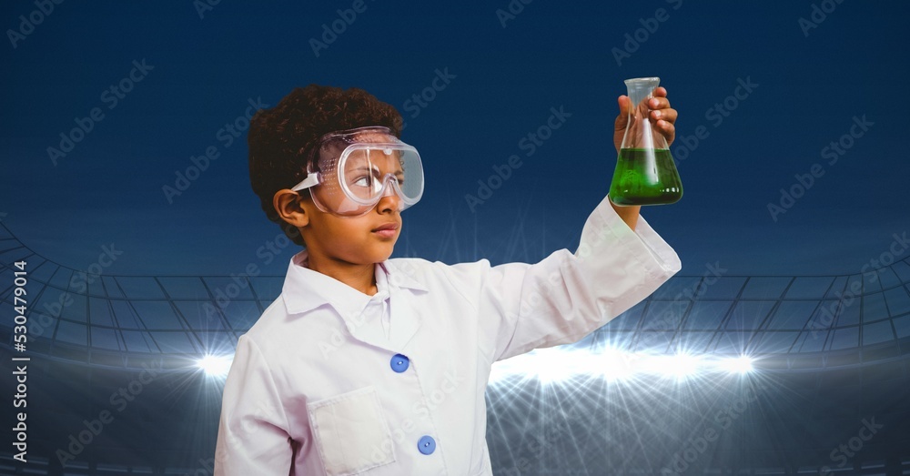 穿着实验服的男孩拿着一个化学烧瓶对着有复制空间的体育场的合成图像