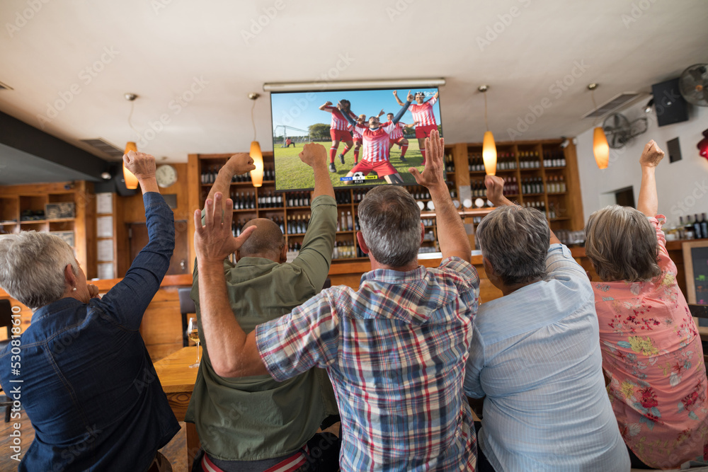 资深多元化朋友在酒吧里支持和看电视，屏幕上有足球比赛