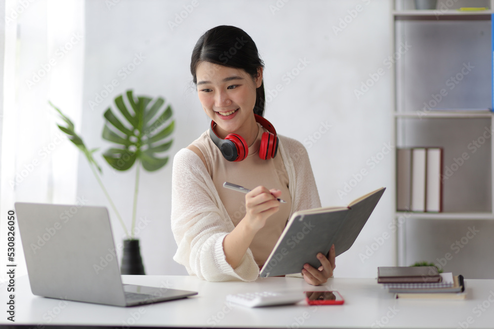 可爱的亚洲少女在家庭办公室用笔记本电脑工作。通过笔记本电脑和网络研讨会进行在线学习。