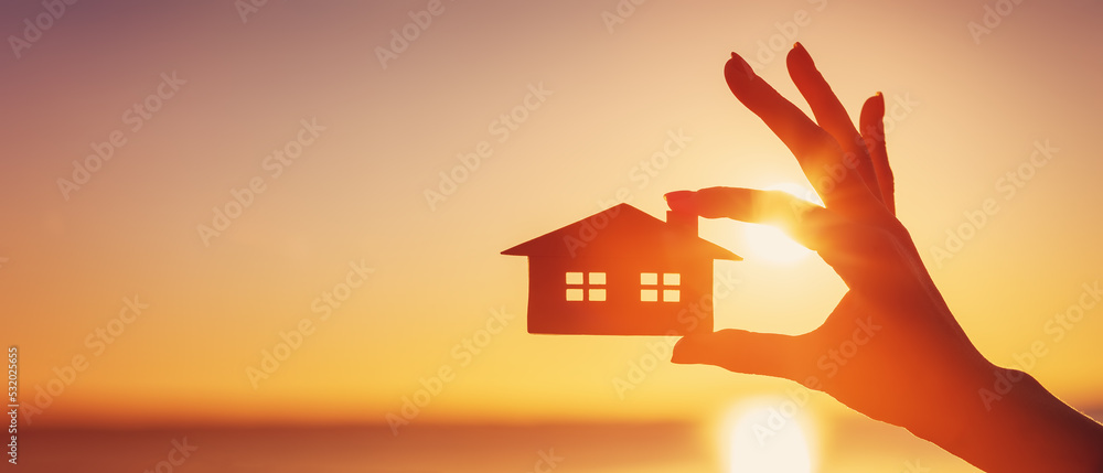 日落之夜，女人手拿着一个房子的模型