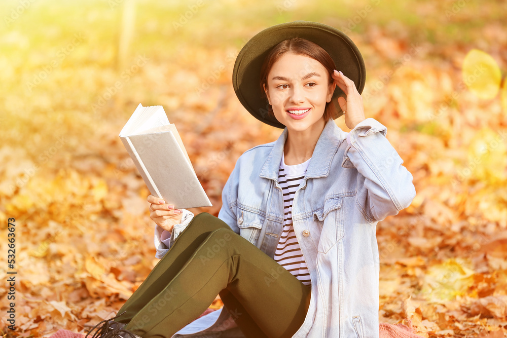 美丽的年轻女子在秋季公园读有趣的书