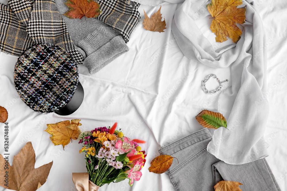 白色织物背景上由秋季服装、配饰和落叶制成的框架