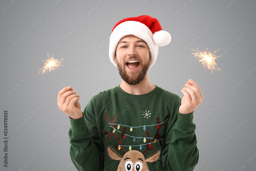 戴圣诞老人帽的年轻人，灰色背景下拿着圣诞亮片