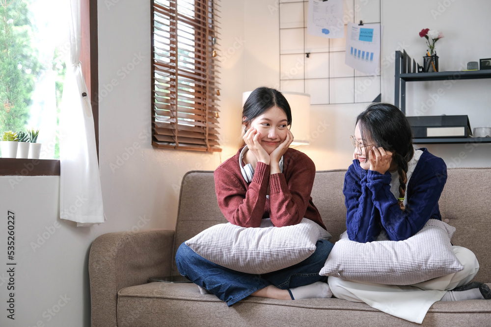 快乐的亚洲女性朋友坐在家里的沙发上。两个年轻的女人在沙发上聊天八卦