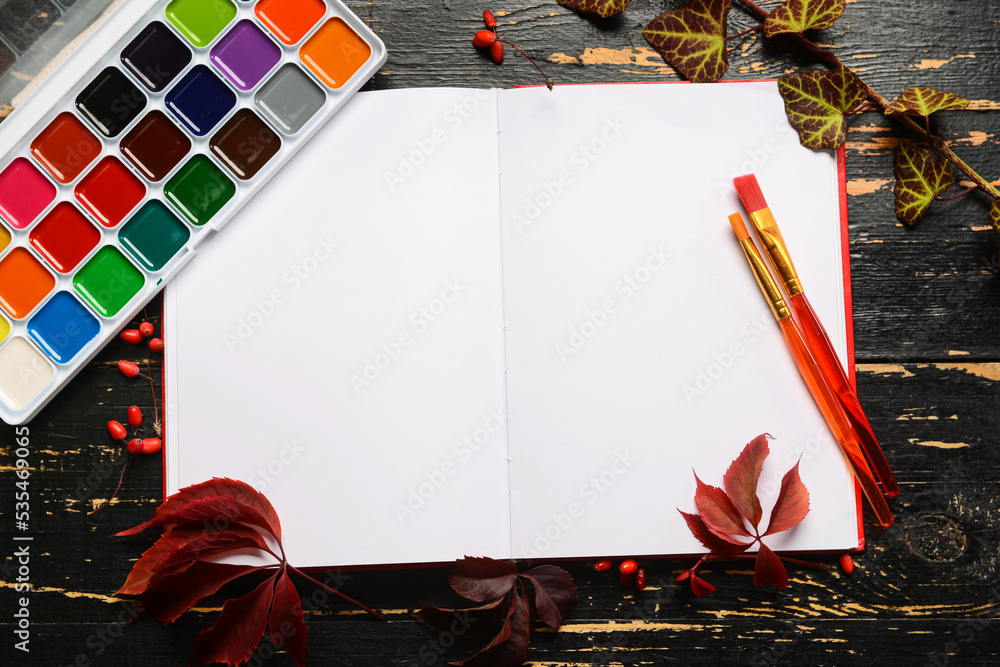 打开笔记本，深色木质背景上的水彩颜料和画笔