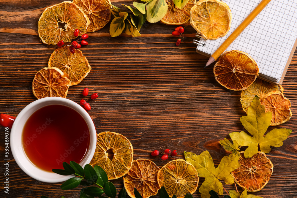 Frame made of notebook, cup of tea and autumn decor on wooden background
