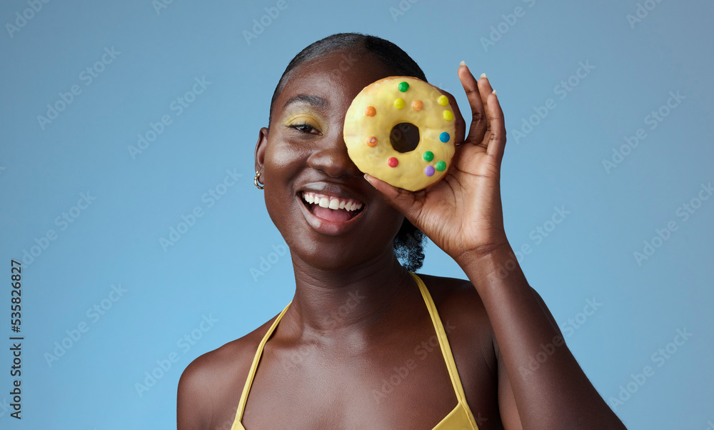 美女，黑人女人，脸上挂着甜甜圈的肖像，蓝色工作室墙，营造夏日快乐的风格。Matc