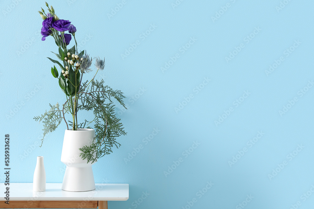 Vases with beautiful ikebana on table near blue wall