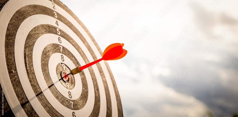 Close up shot red darts arrows in the target  of dartboard center on dark blue sky background. Busin
