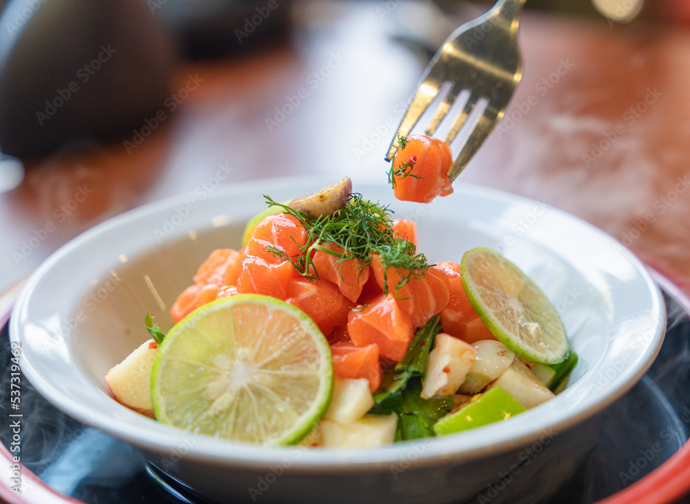 Spicy sliced salmon with fruit salad in white ceramic bowl