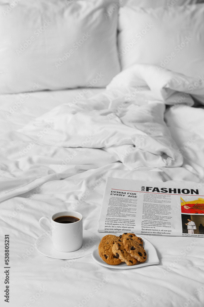 Plate with sweet cookies, cup of coffee and newspaper on bed