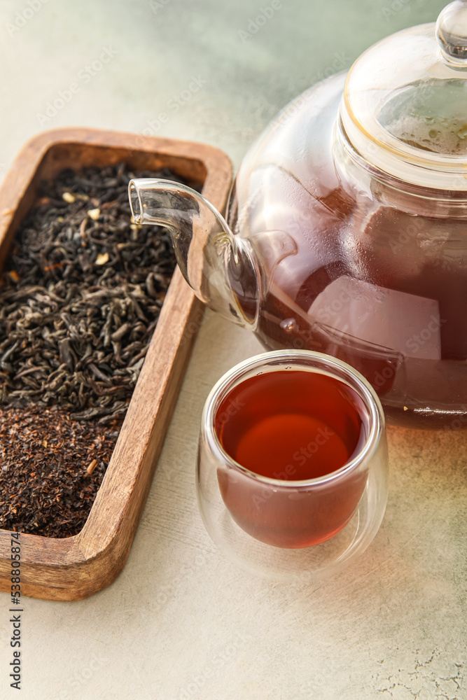 一杯芳香的红茶、茶壶和干叶，背景为浅色，特写