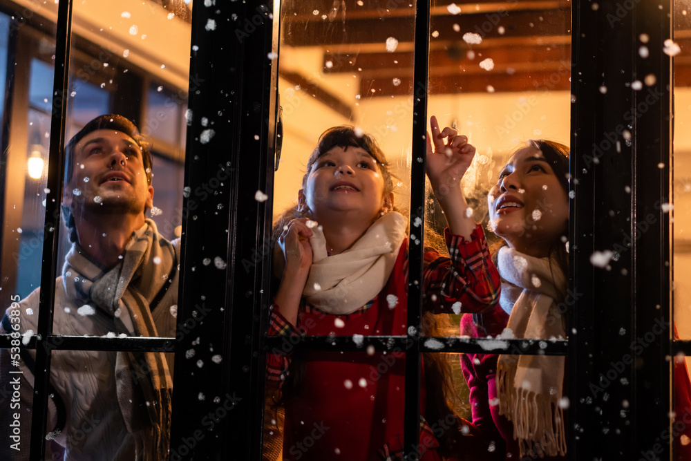 可爱的孩子看着窗户，和家人一起吃第一片雪花