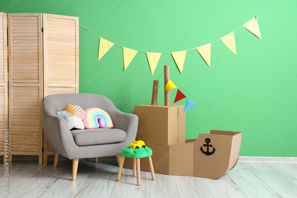 儿童房内部，靠近绿色墙壁的玩具纸板船和扶手椅