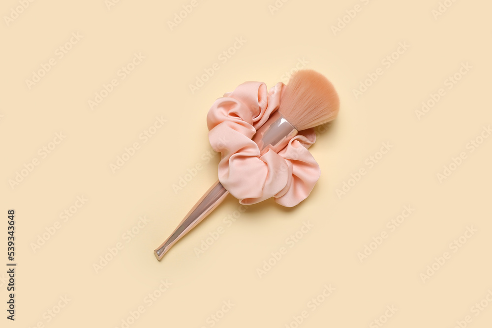 Makeup brush and silk scrunchy on color background