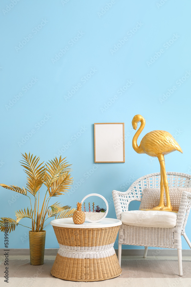 房间蓝色墙壁附近有金色火烈鸟的扶手椅、桌子和空白相框