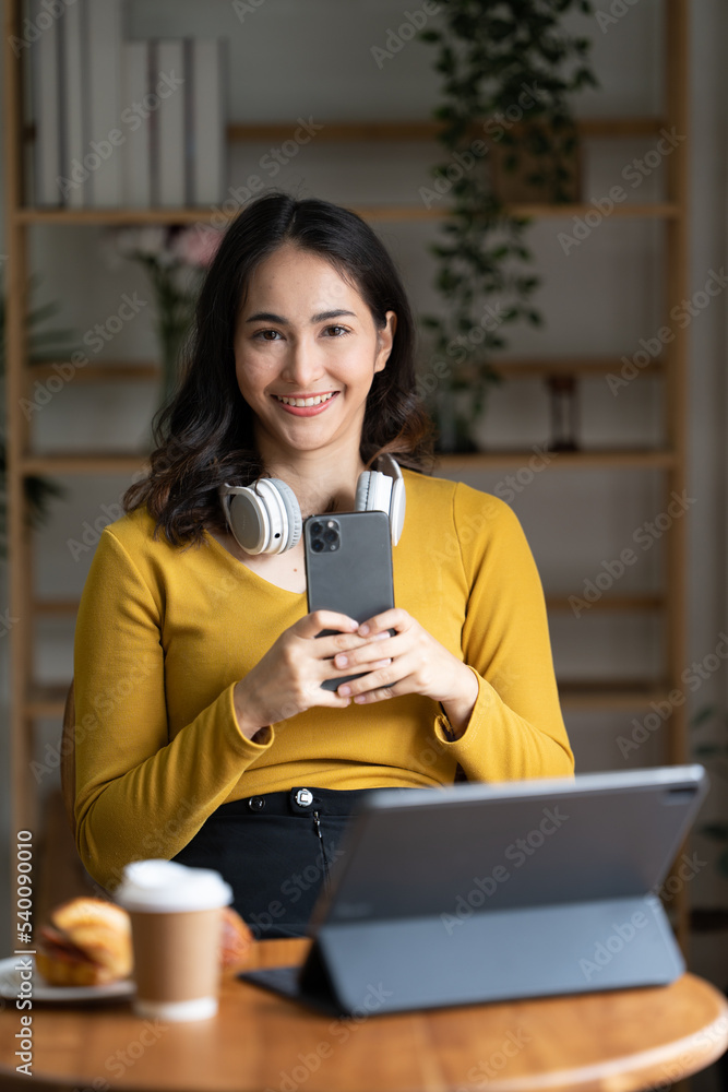 美丽的年轻亚洲女商人拿着咖啡杯和笔记本电脑在办公室工作，面带微笑。