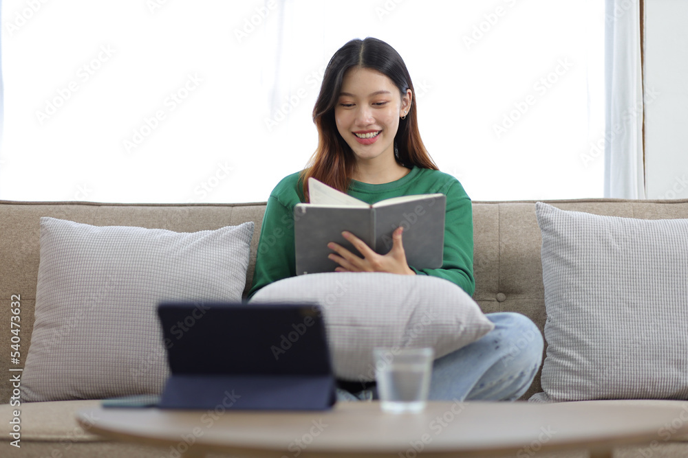 漂亮的亚洲女人坐在沙发上看书。