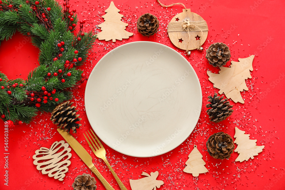 红色背景上的盘子、圣诞装饰品、花环和圆锥体组成