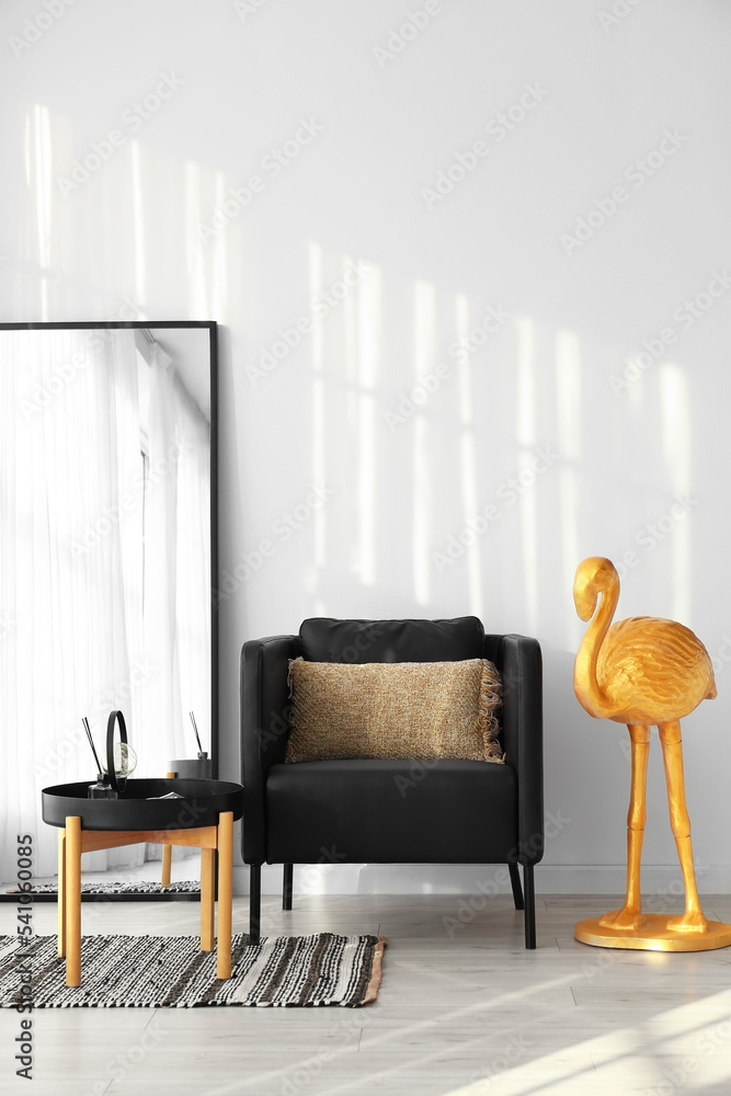 Comfortable armchair, mirror and golden flamingo near light wall in room interior