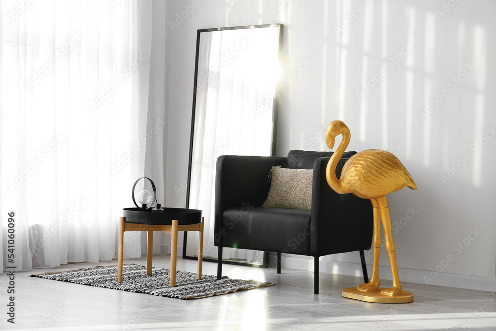 Comfortable armchair, mirror and golden flamingo near light wall in room interior