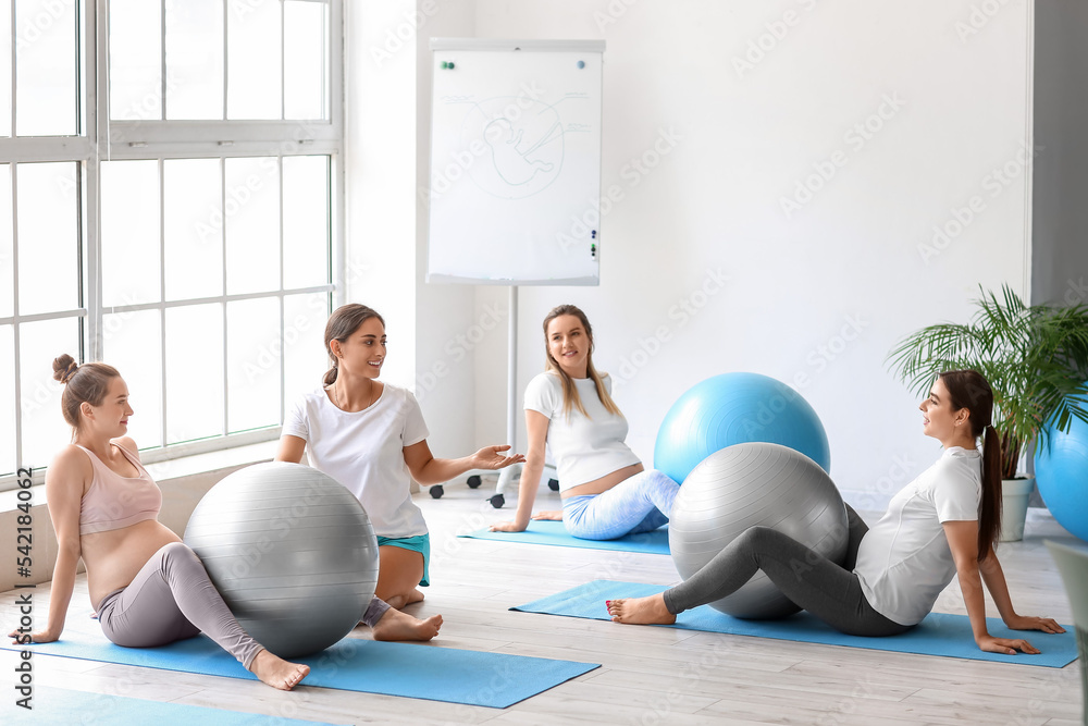 年轻孕妇在健身房与教练和健身球一起做瑜伽