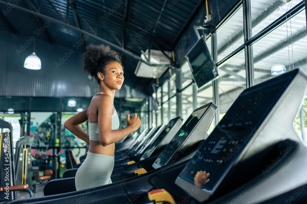 非洲裔美国年轻女运动员在健身房的跑步机上跑步。