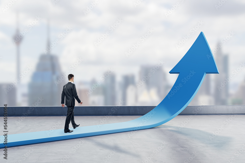 Young businessman walking on abstract upward blue arrow on blurry city background. Growth, career an