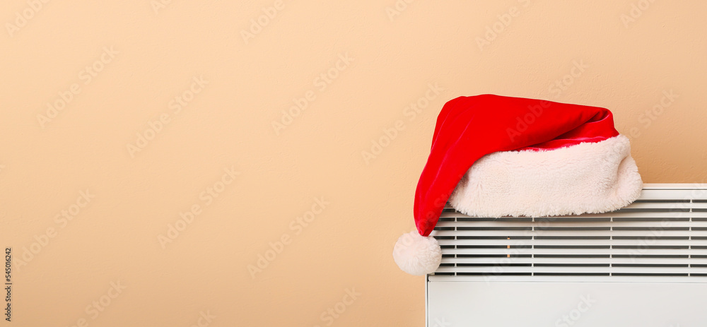 米色墙壁附近的电散热器上的圣诞老人帽，有文字空间