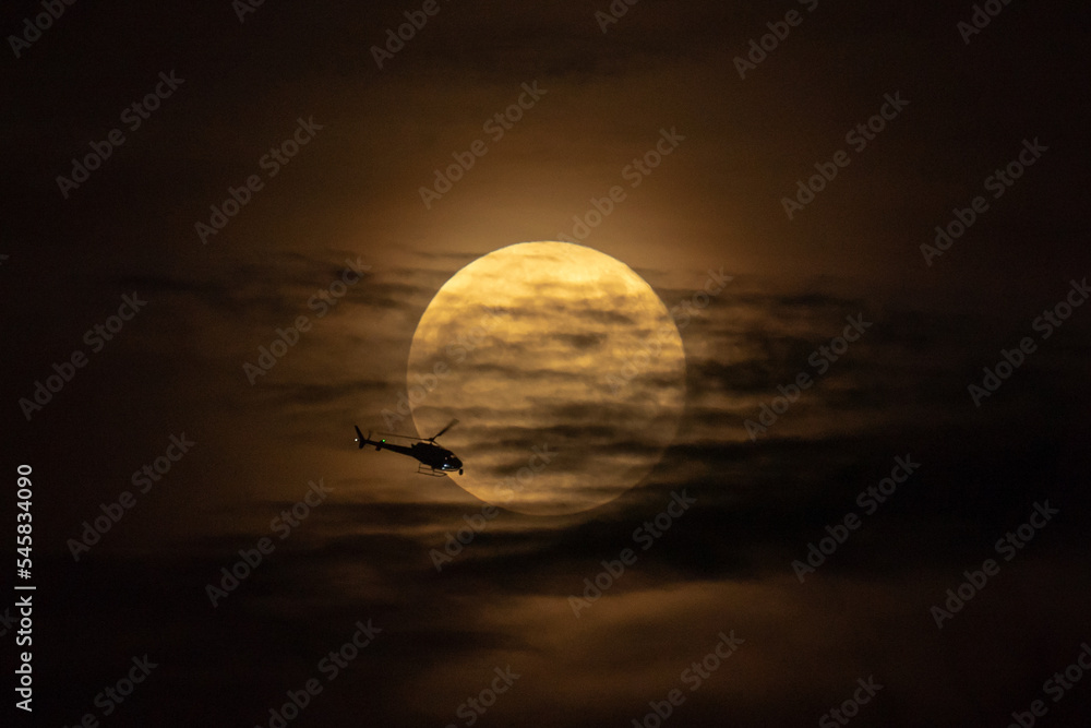 直升机在夜间飞越满月。背景满月上有直升机光环