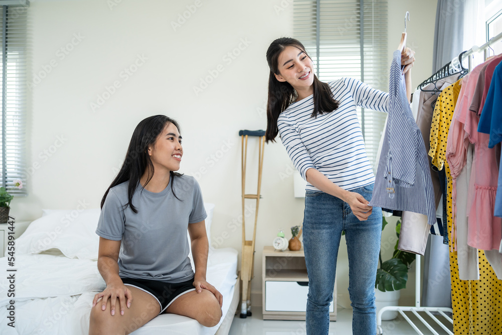 亚洲年轻截肢者腿女人和朋友在壁橱架子上挑选衣服。