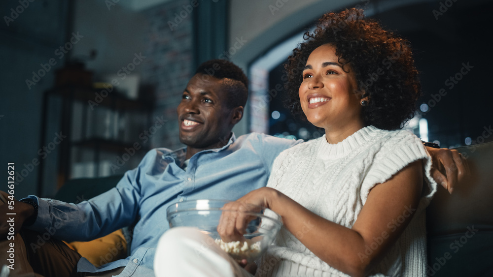 黑人夫妇在电视上看喜剧电影，坐在公寓的沙发上吃爆米花