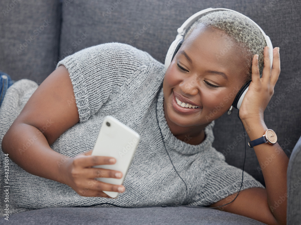 黑人女性，坐在沙发上的家庭客厅里，音乐和电话视频流媒体很开心。社交媒体应用程序