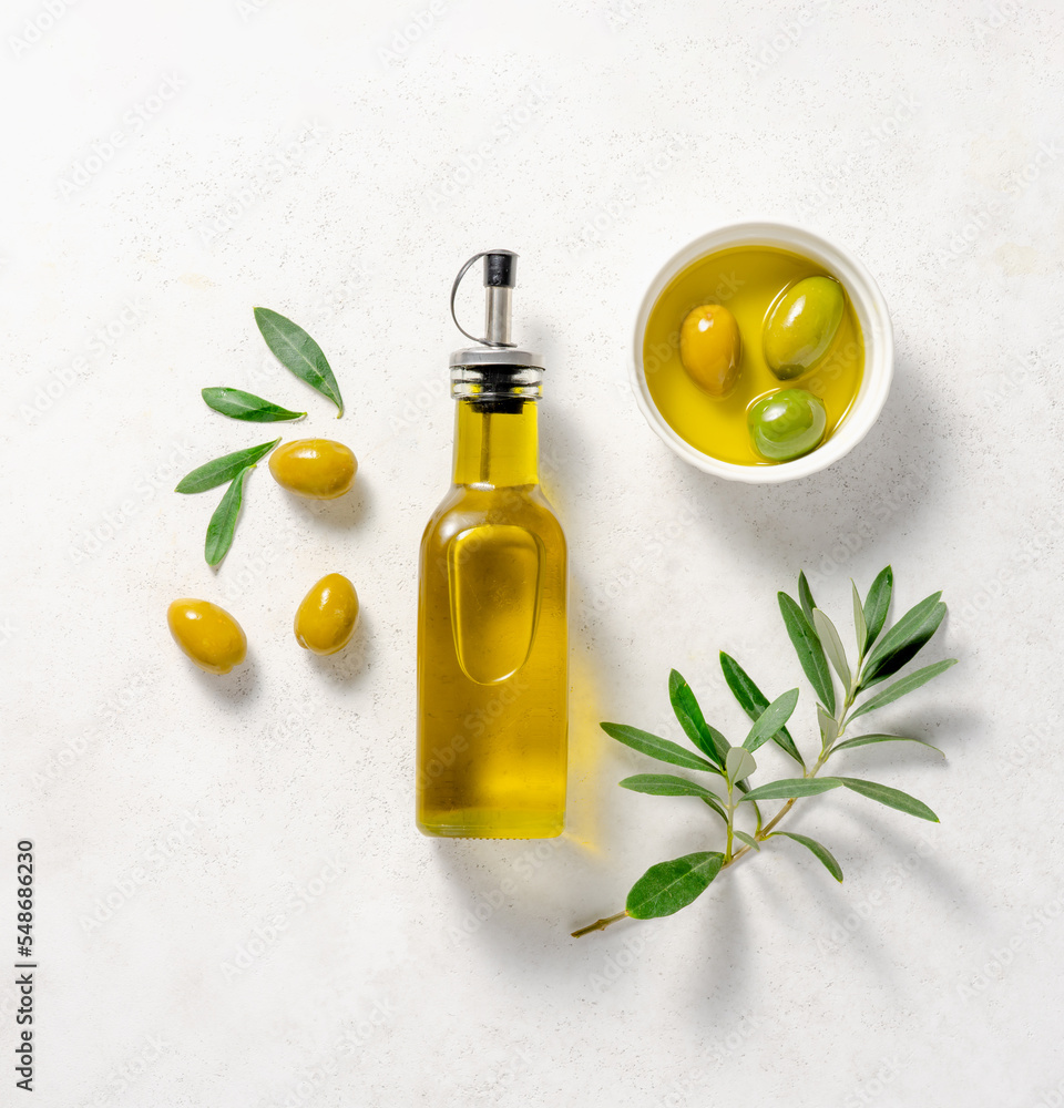 白碗里的橄榄和橄榄油。一瓶白底橄榄叶的橄榄油。Mocku
