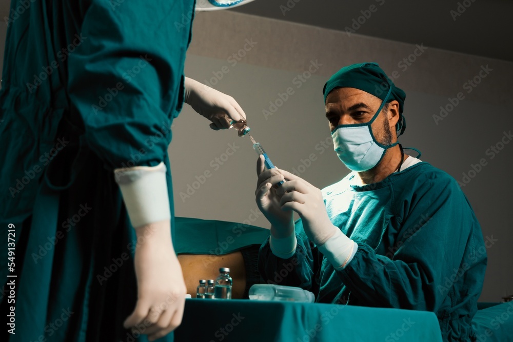 外科医生在无菌手术室用助手从医用小瓶中填充注射器进行手术