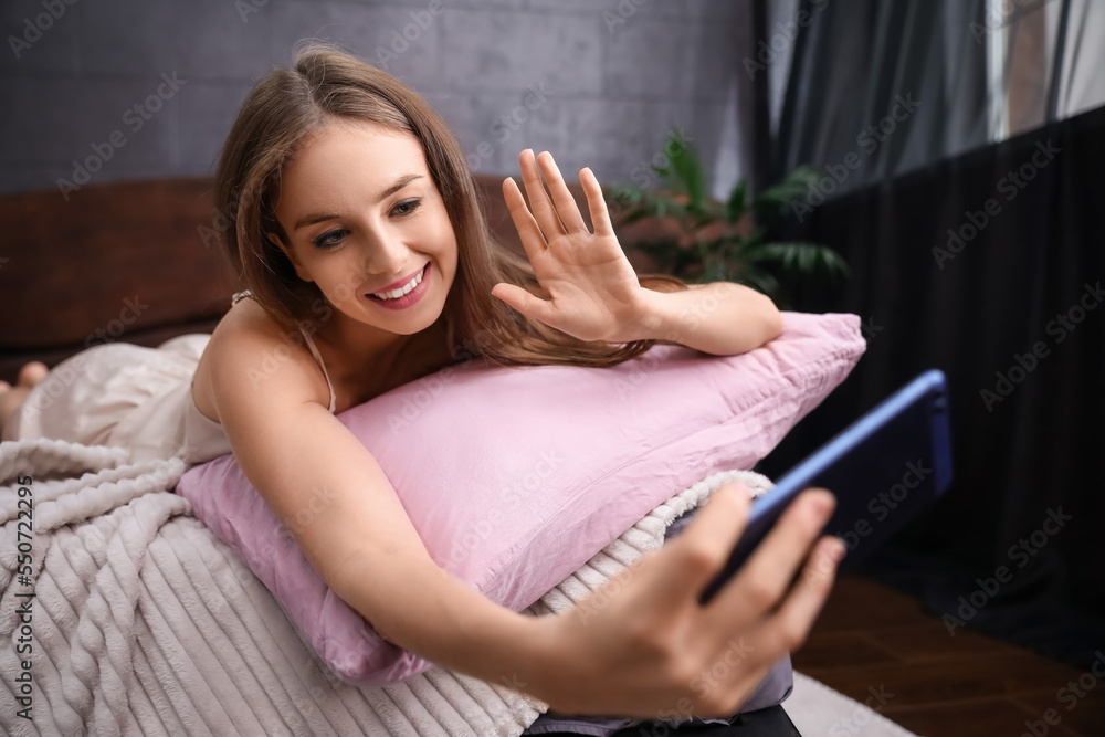 Pretty young woman taking selfie on bed at home