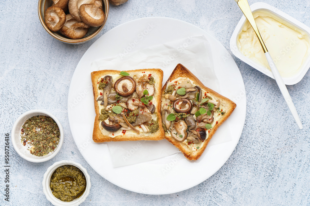 Plate of tasty toasts with cream cheese, mushrooms and pesto sauce on light table