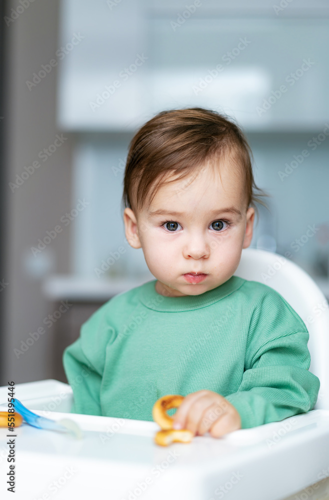 Small child sits on a chair and eating with spoon. Baby boy eats